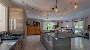 A modern kitchen with a large island, wooden cabinets, and pendant lighting. - Holiday Home with Spa and Pool (montrem)