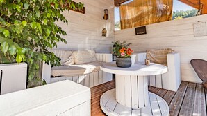 A wooden deck with a round table, white cushioned seating, and a potted plant with flowers. - Holiday Home with Spa and Pool (montrem)
