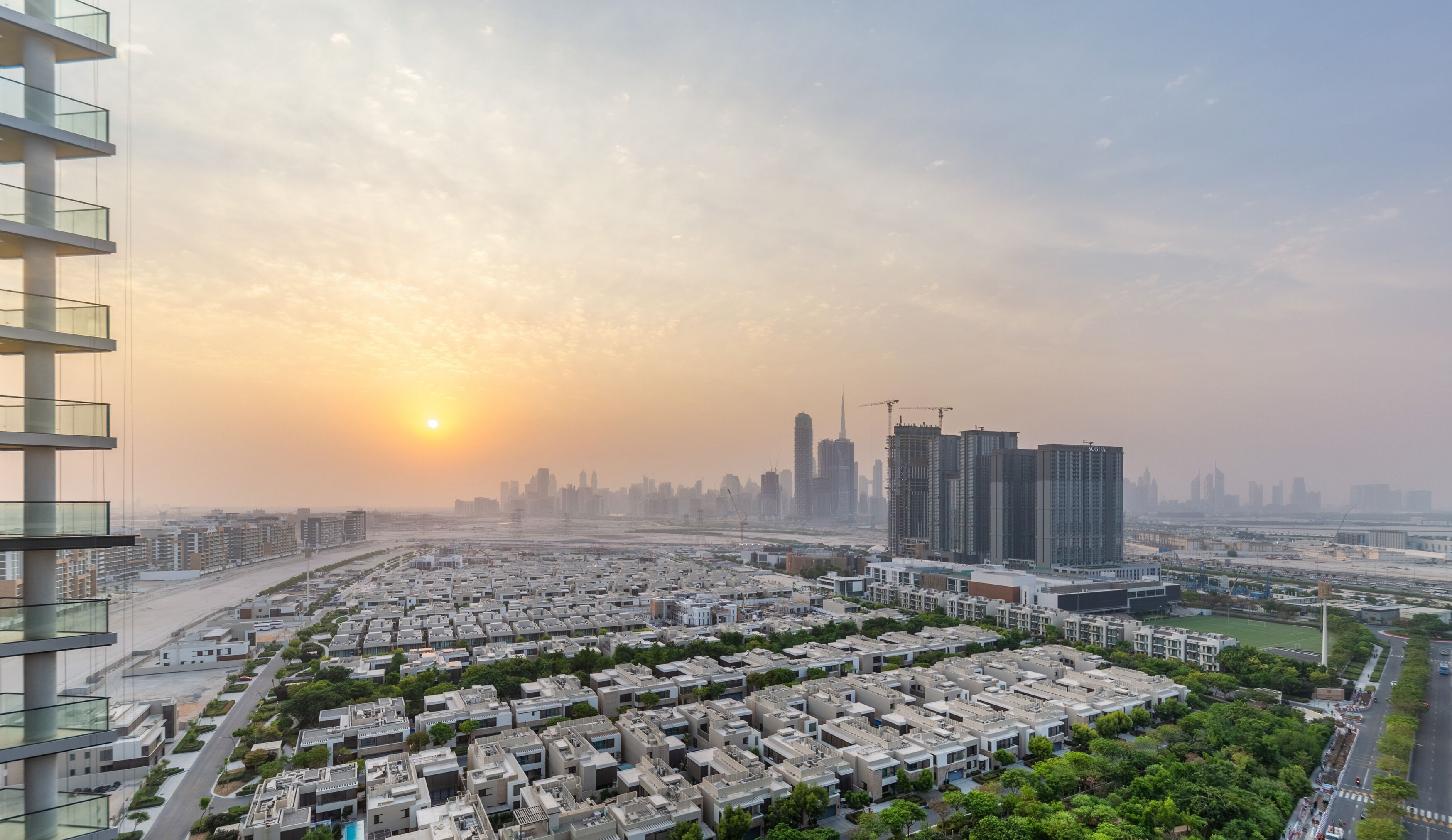 A high-rise building with multiple balconies overlooking a cityscape during sunset.