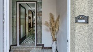 Entrada de un hotel con puerta de cristal, un jarrón blanco con plumas de pampa y un cartel que dice 'Can Mateu'.