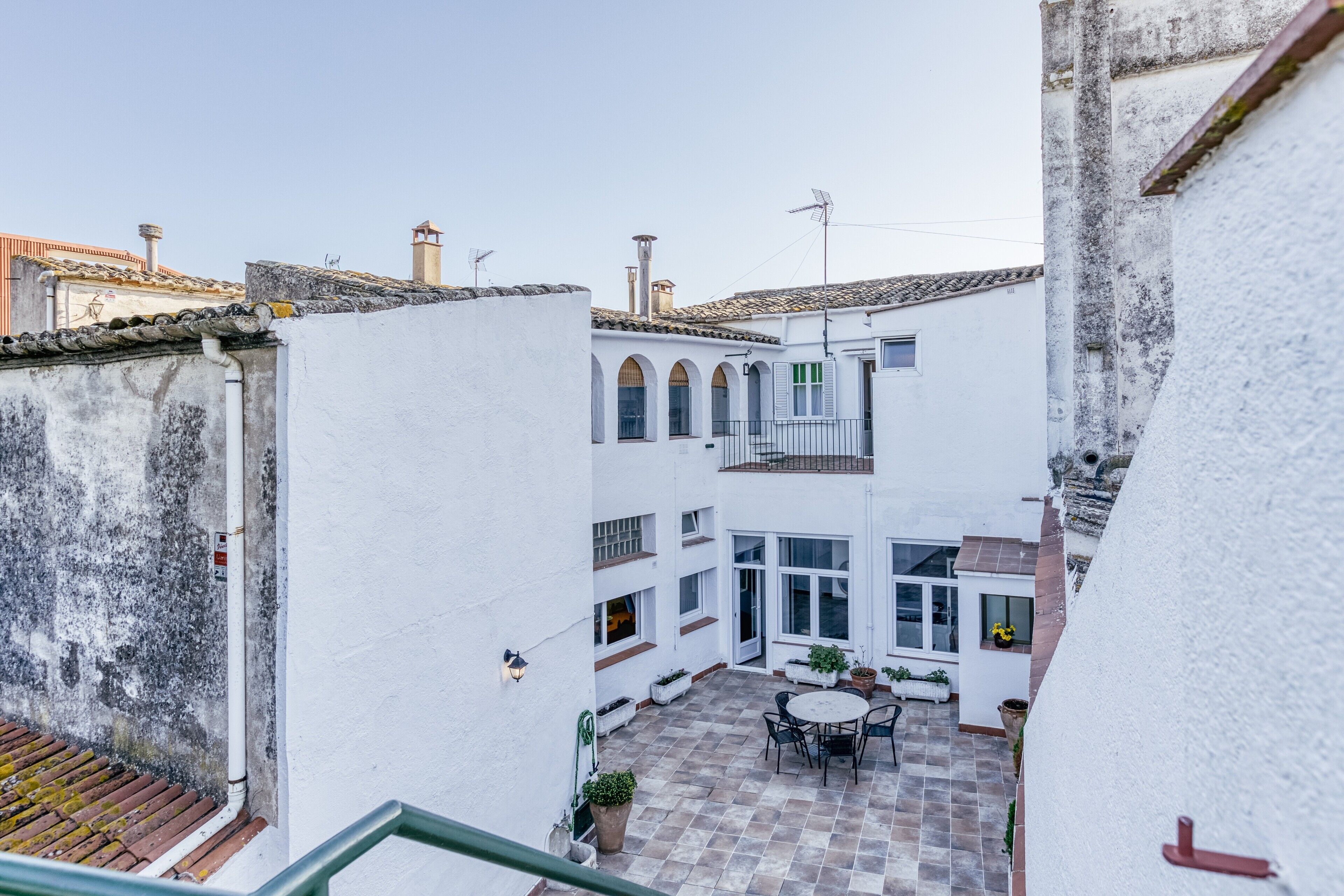 Une cour avec une table ronde et des chaises, un petit jardin et un bâtiment blanc doté d’un balcon.