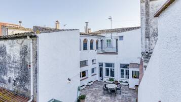 Une cour avec une table ronde et des chaises, un petit jardin et un bâtiment blanc doté d’un balcon.