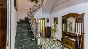 Una escalera con barandilla, un banco de madera, un jarrón con plantas secas y un espejo con marco decorativo.