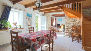 A dining area with a table set for four, wooden chairs, a chandelier, and a stone wall in the background. - Maison de pecheur en pierres  bord de mer 300 m (Pleubian)
