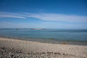 A pebbly beach with calm water and distant land.