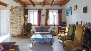 A cozy living room with a stone wall, wooden ceiling beams, a sofa, chairs, a television, and a fireplace. - Maison de pecheur en pierres  bord de mer 300 m (Pleubian)