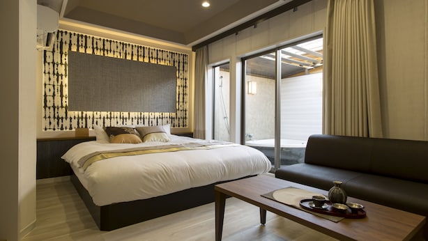 Une chambre d’hôtel moderne, dotée d’un grand lit, d’un canapé, d’une table basse en bois et offrant une vue sur l’extérieur.