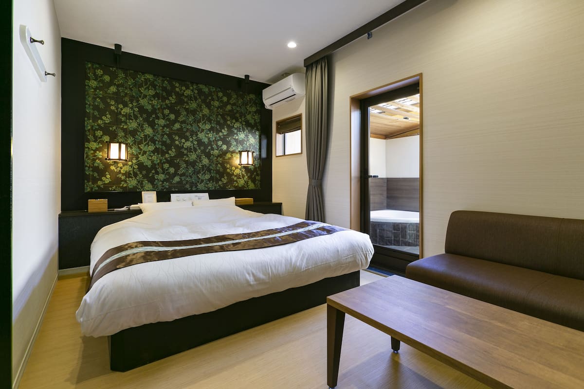 Een moderne hotelkamer met een groot bed, een houten nachtkastje, een houten tafeltje, een bank en een decoratieve wand, plus een raam met gordijnen.