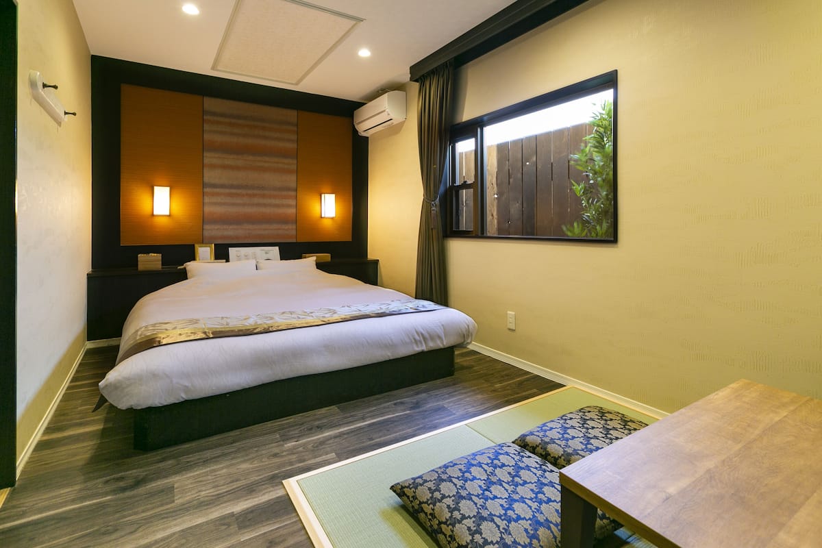 Een hotelkamer met een groot bed, twee nachtkastjes, een kleintje en een raam met gordijnen.