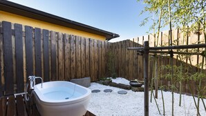 Une terrasse en bois avec un jacuzzi, une clôture en bois et un espace jardin agrémenté de galets blancs et de plantes en bambou.