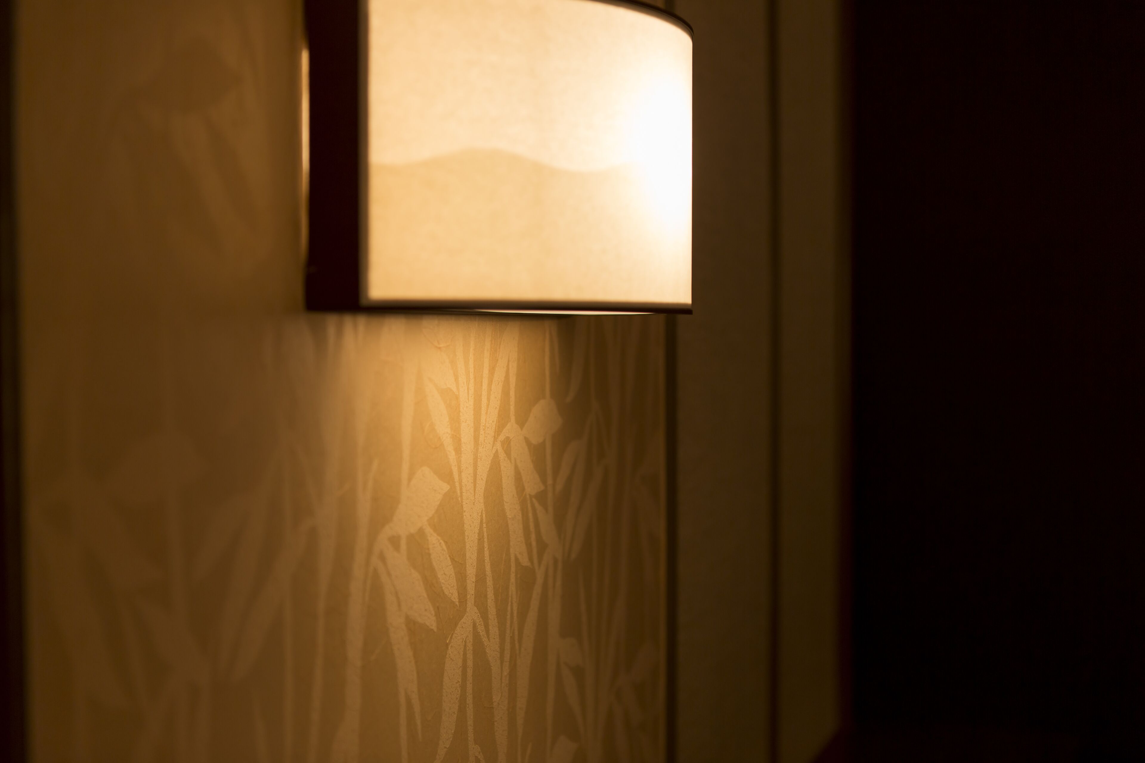A wall-mounted lamp with a rectangular shade and a patterned wall behind it.
