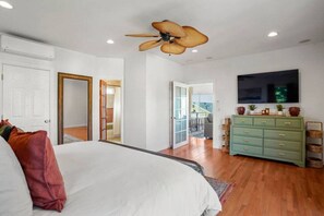 A bedroom with a bed, a green dresser, a ceiling fan, and a TV mounted on the wall.