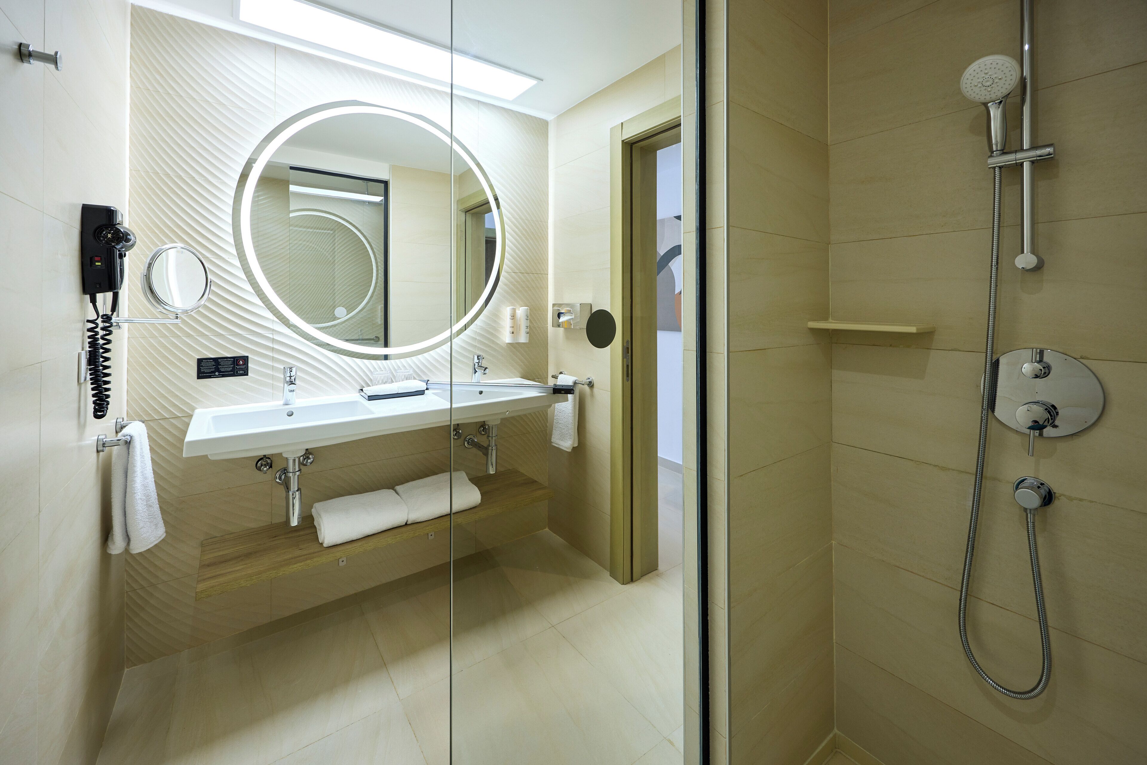 A modern bathroom with a glass-enclosed shower, a round mirror, a white sink, and a towel rack.