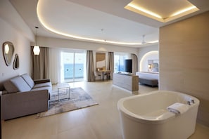 A modern hotel room with a large bathtub, a sofa, a dining area, and a TV.