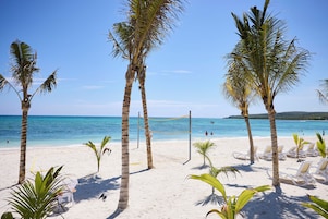 A beach with white sand, palm trees, and a volleyball net.