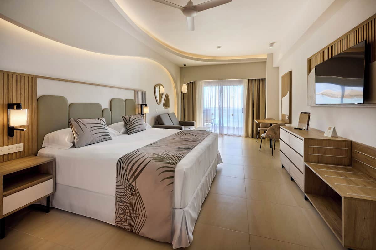 A modern hotel room with a large bed, bedside tables, a desk, and a TV.