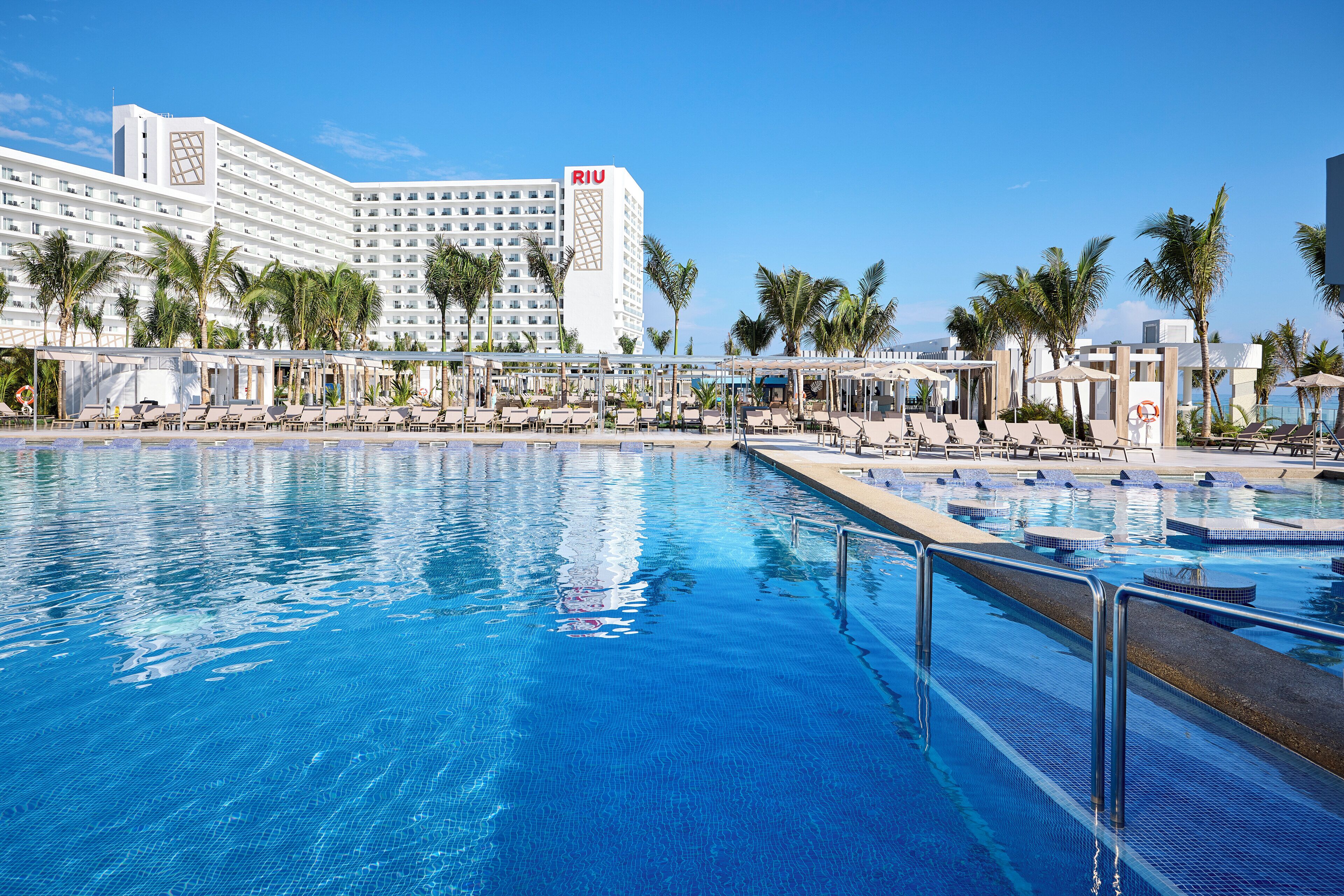 A hotel with a large pool area, palm trees, and a clear blue sky.