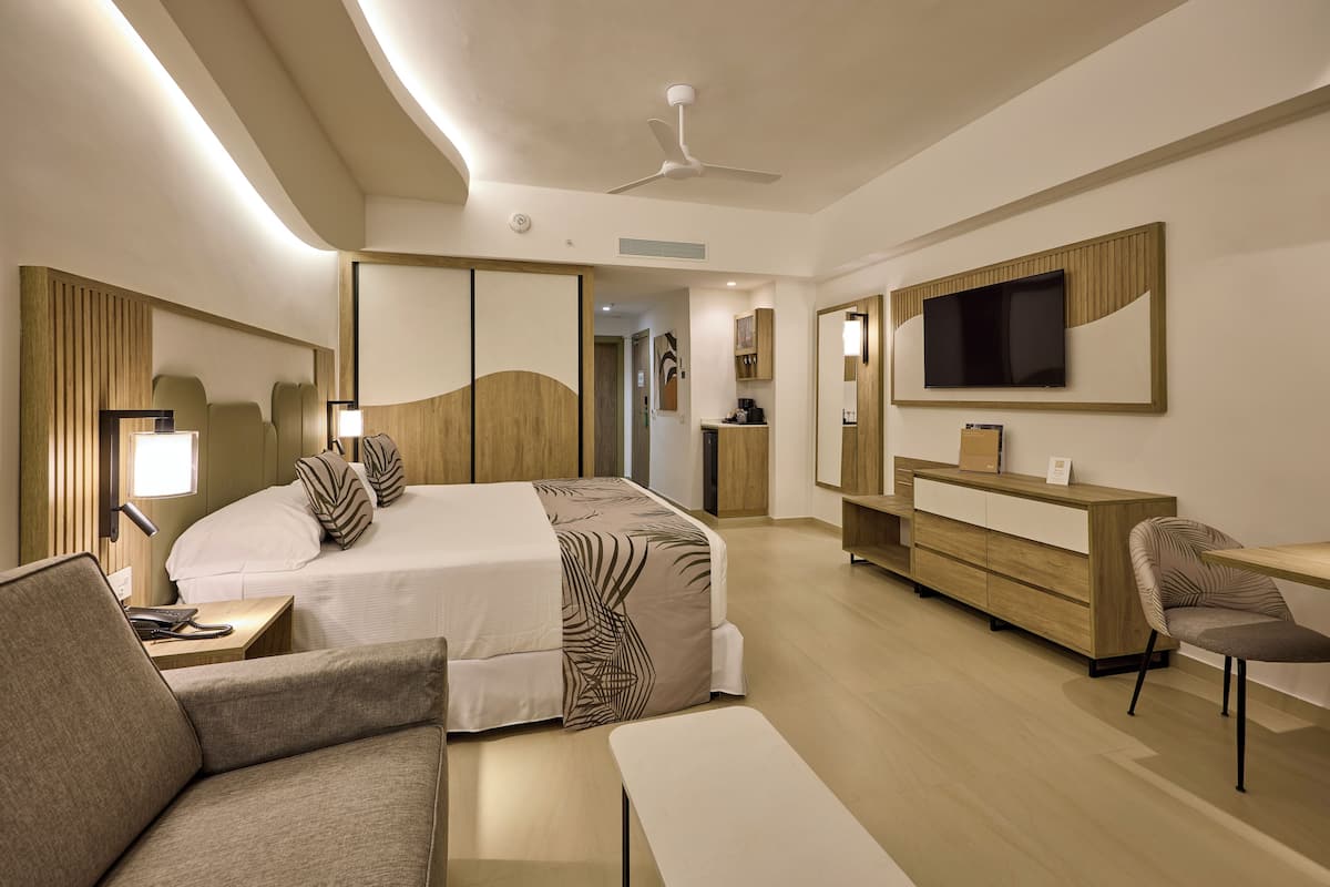 A modern hotel room with a large bed, a desk, a chair, and a TV.