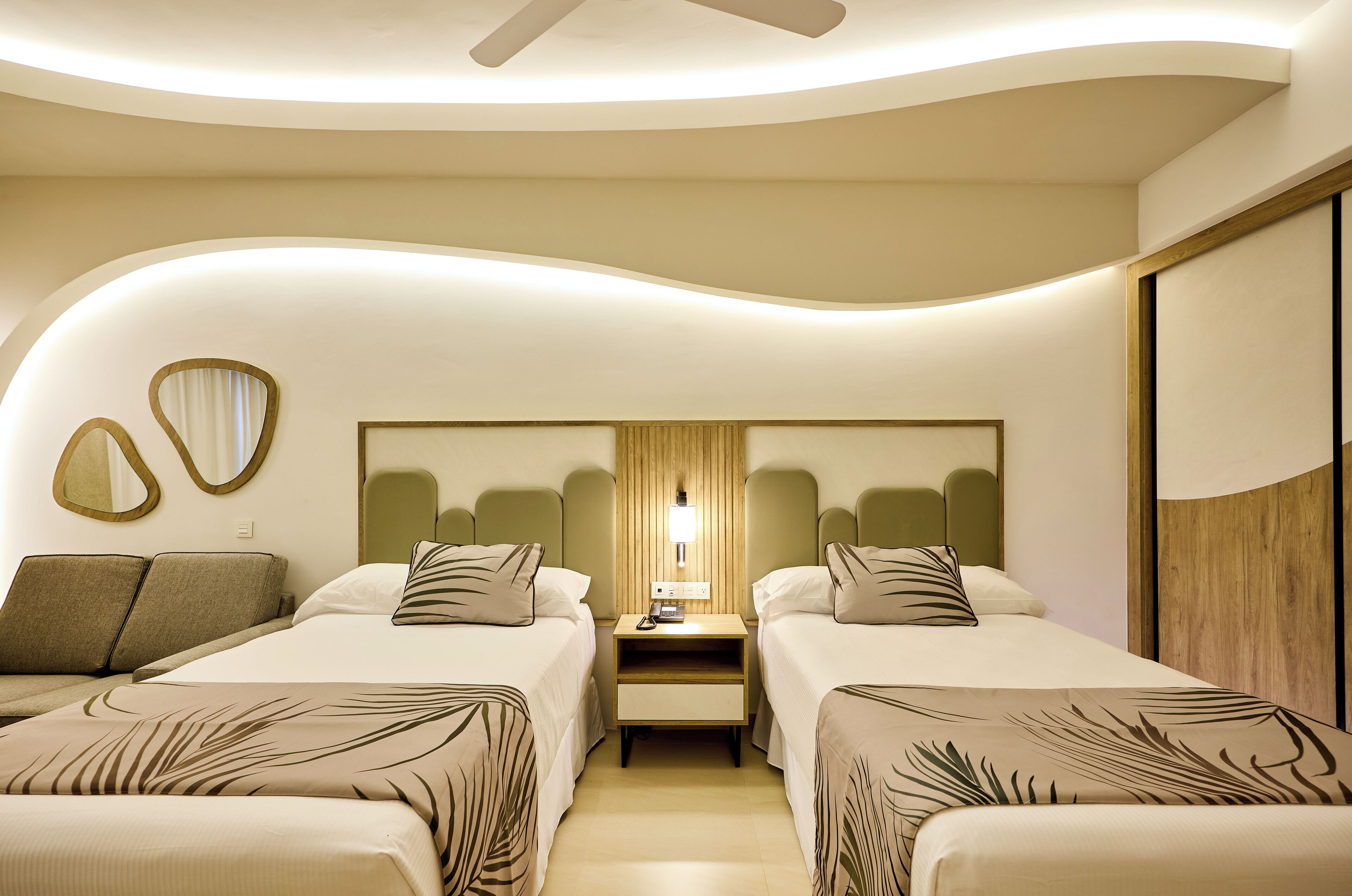 Habitación de hotel con dos camas, una mesita de noche, un espejo y un ventilador de techo.