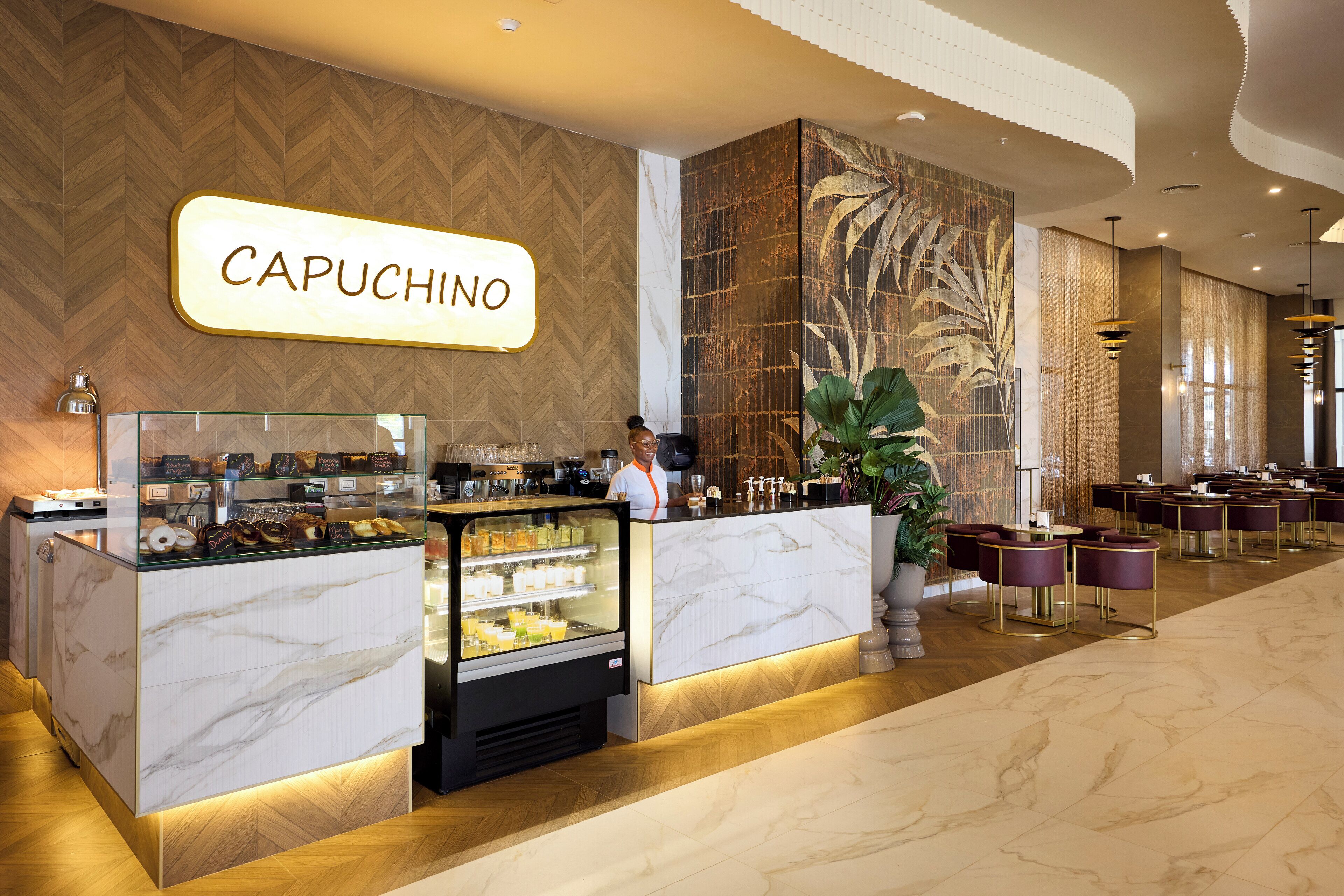 A cafe area with a marble counter, a refrigerated display case, and a sign that reads "CAPUCHINO".