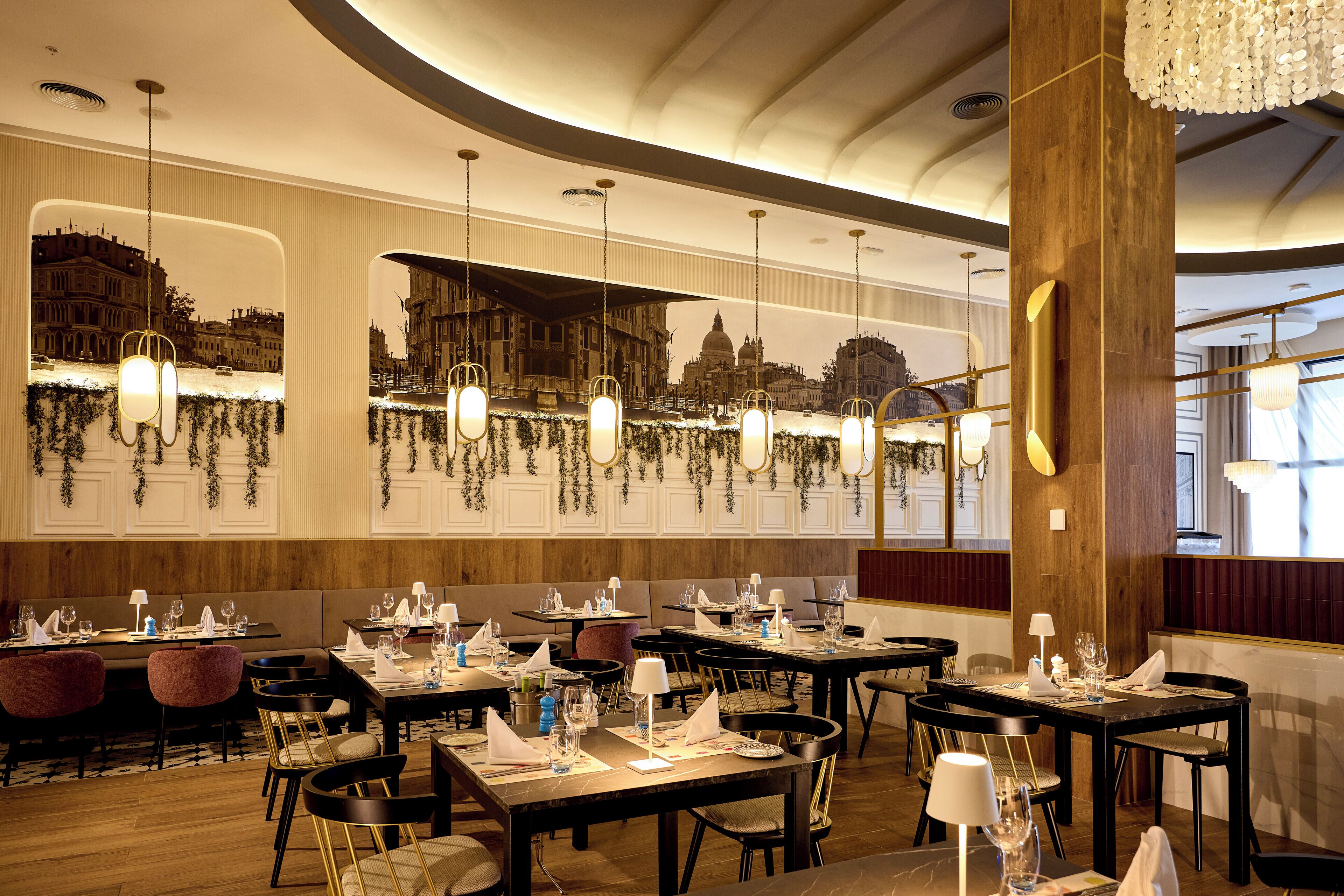 A restaurant with multiple tables set for dining, featuring a cityscape mural on the wall and hanging pendant lights.