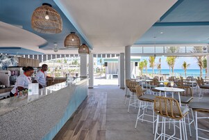 Zona de bar moderna con barra, taburetes y lámparas de mimbre colgantes.