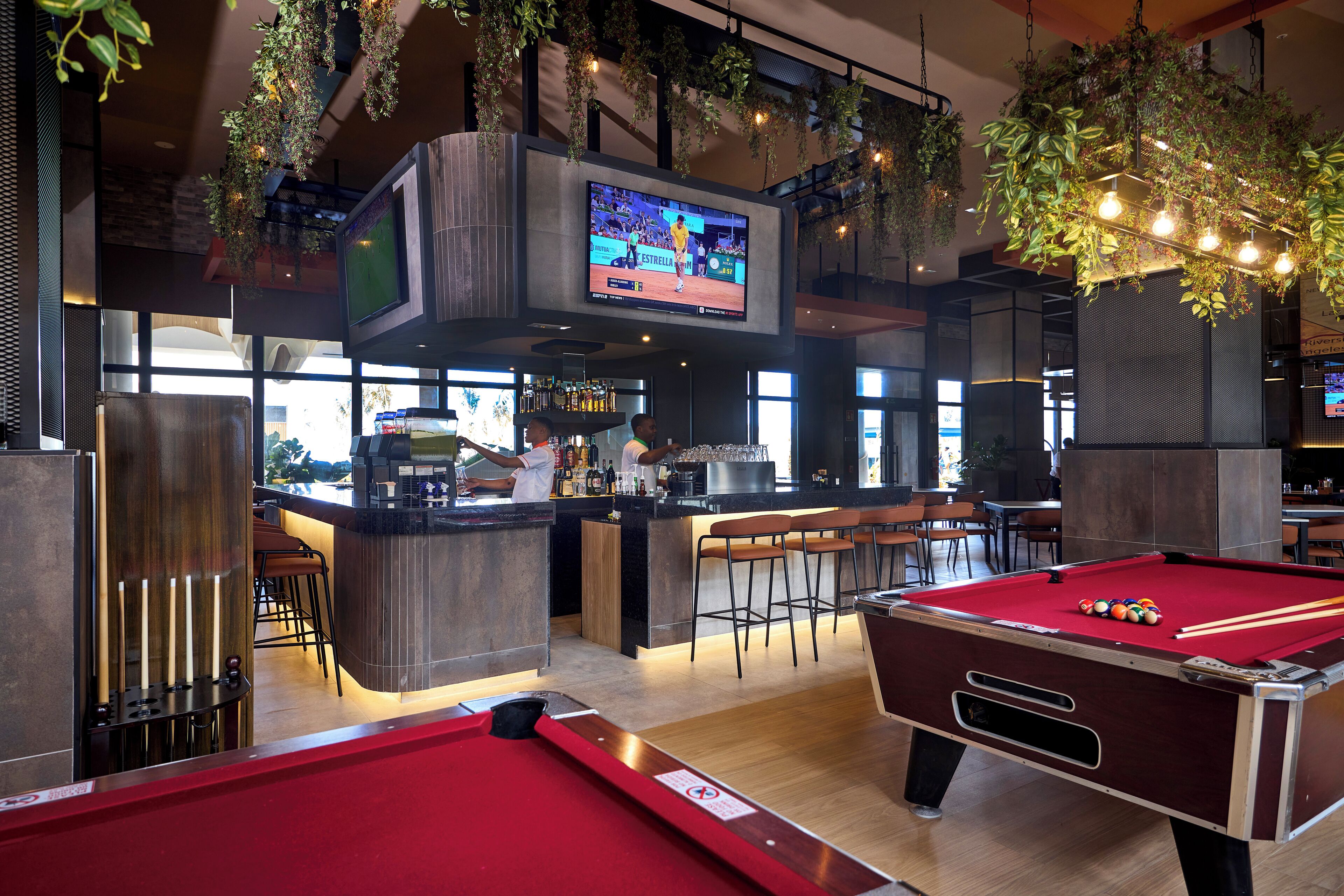 A pool table, a bar area, and a television screen in a modern indoor setting.