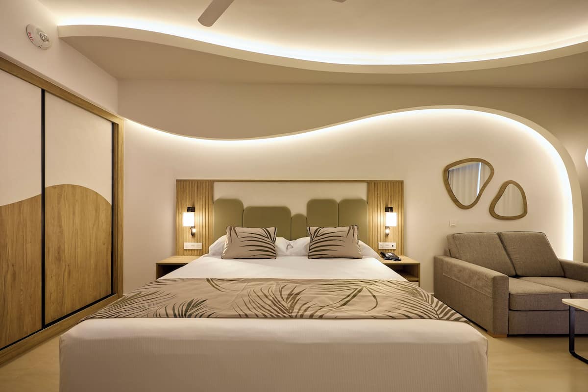 A modern hotel room with a large bed, a sofa, and a curved ceiling design.