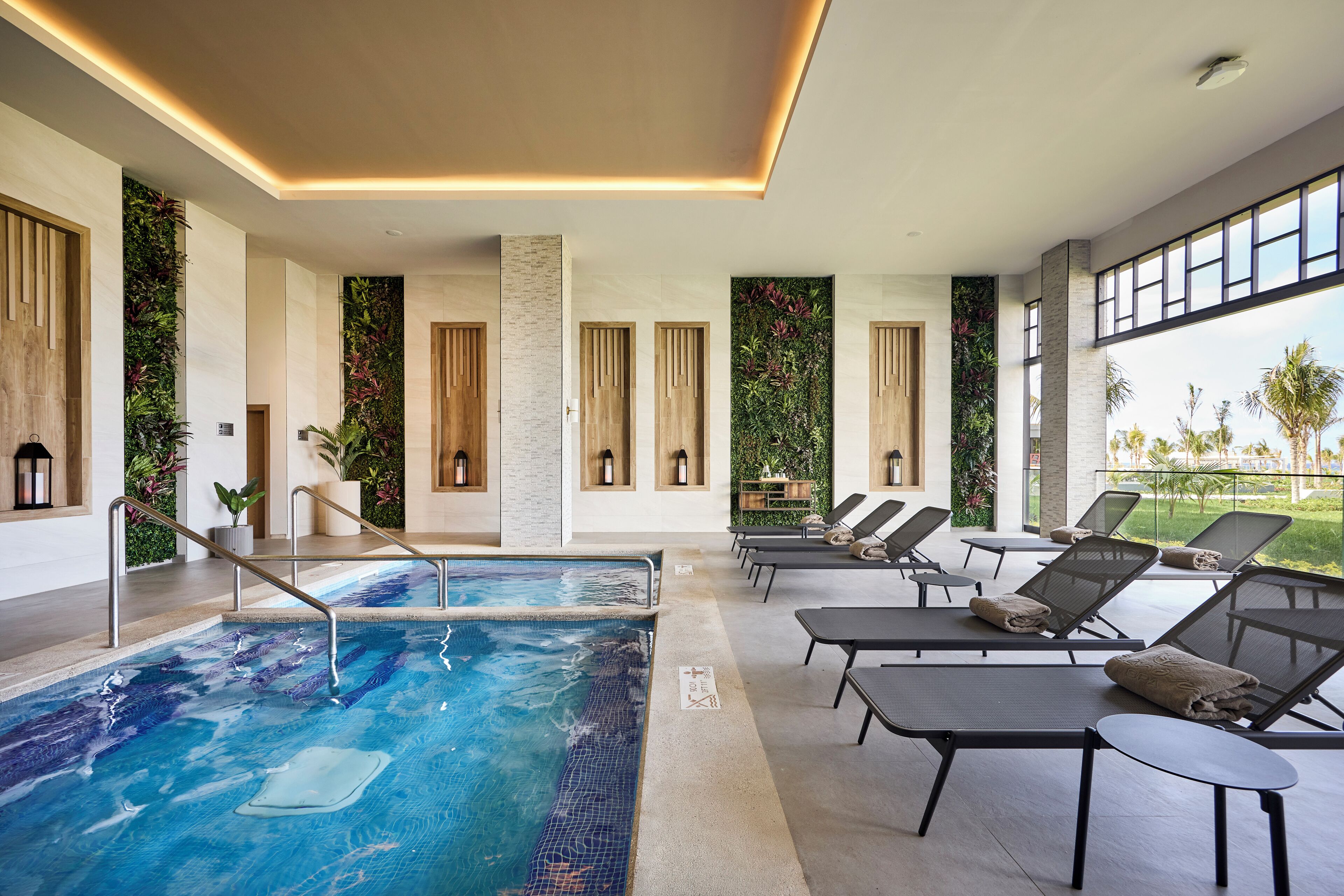 Een modern binnenzwembad met helder water, lounge stoelen en uitzicht op het buitengebied.