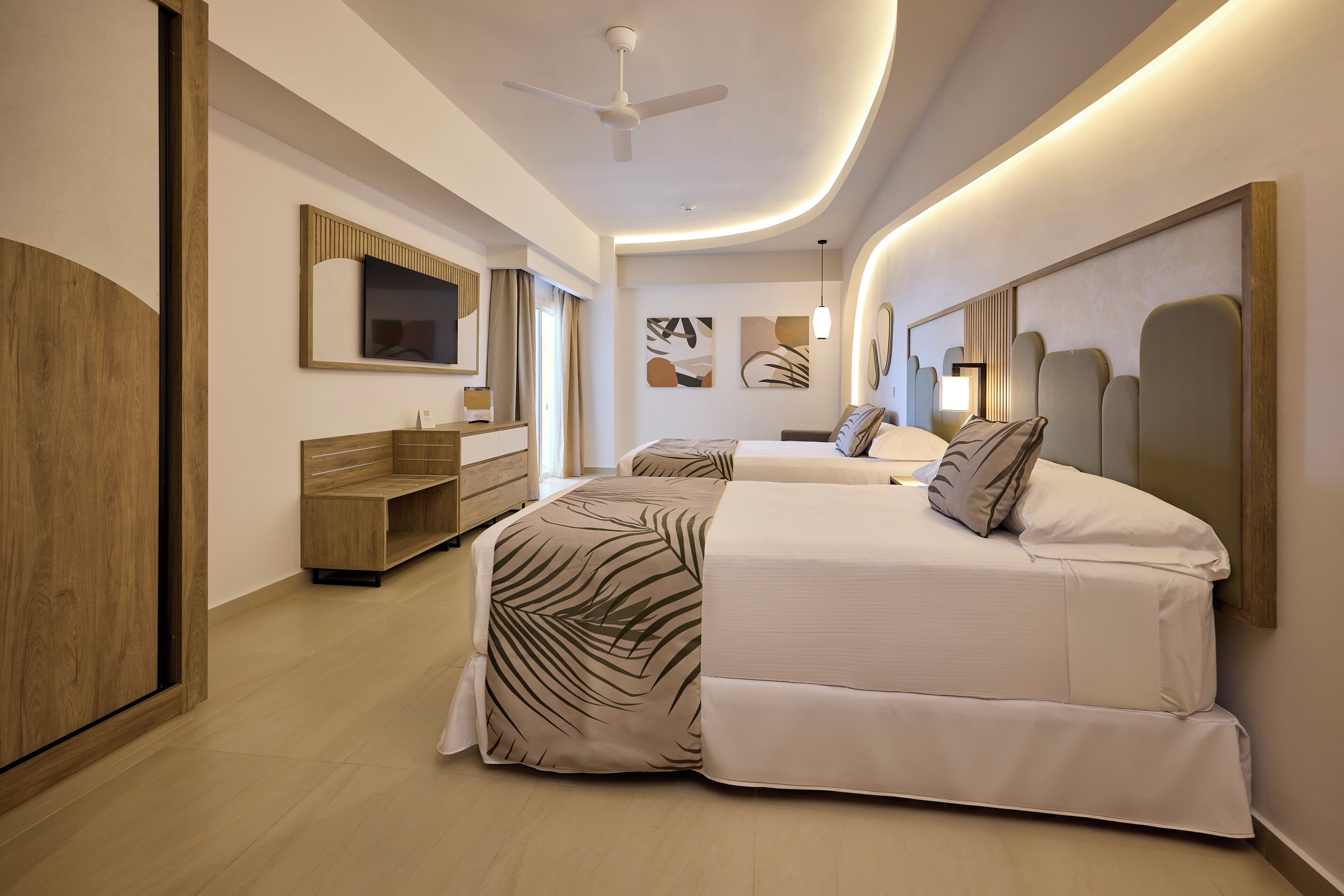 Une chambre d’hôtel moderne avec deux lits, une télévision, un banc en bois et des œuvres d’art abstraites accrochées au mur.