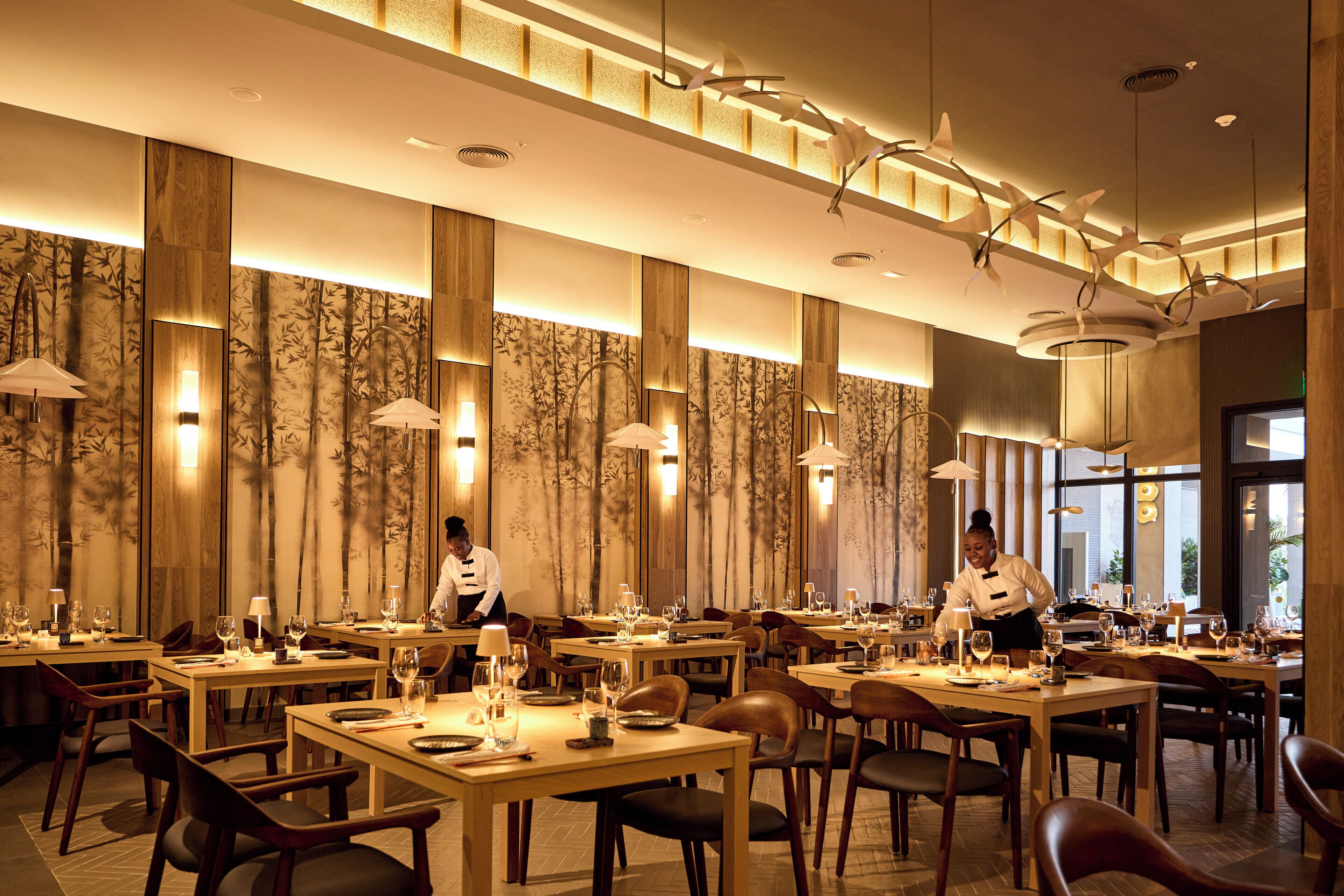 A restaurant with multiple tables, chairs, and overhead lighting fixtures.