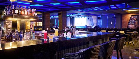 A bar area with a counter displaying various bottles and glasses, wicker bar stools, and a seating area with tables and chairs.