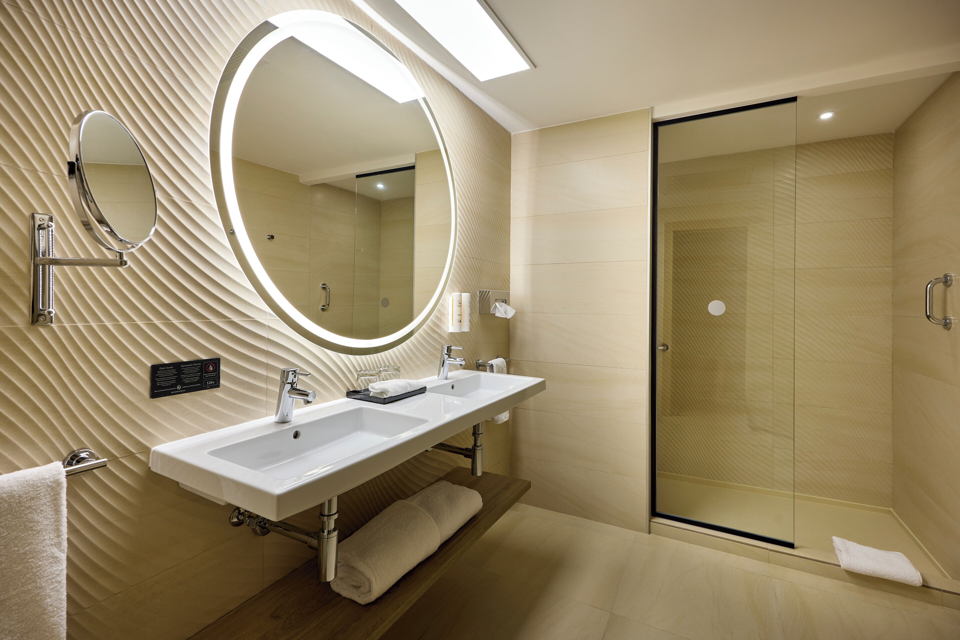 Een moderne badkamer met een grote spiegel, twee wastafels en een douchecabine van glas.