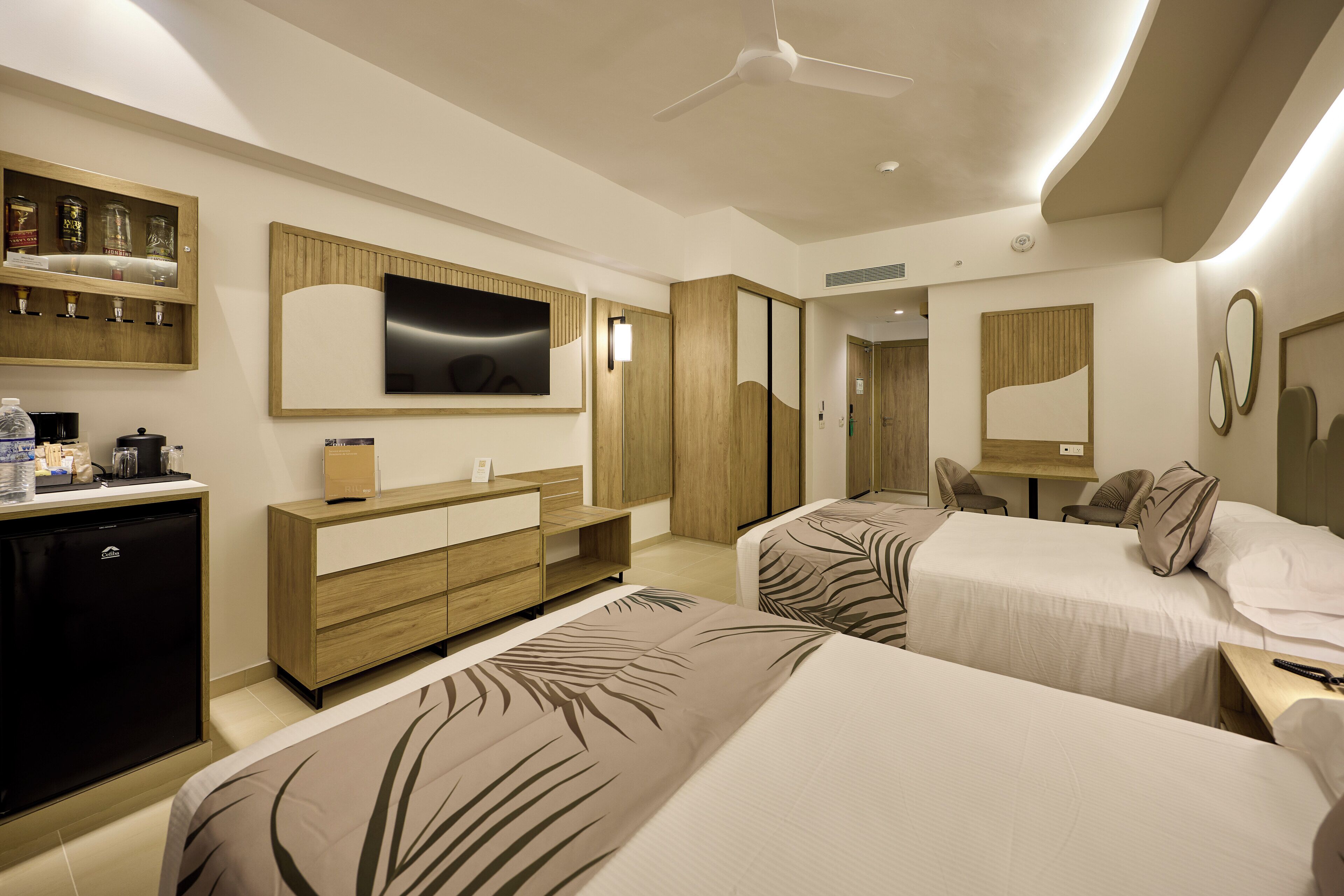 Une chambre d’hôtel avec deux lits, une télévision, un minibar et un bureau avec une chaise.