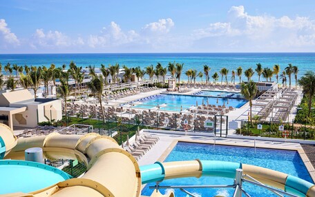 A resort with multiple swimming pools, palm trees, and a view of the ocean.