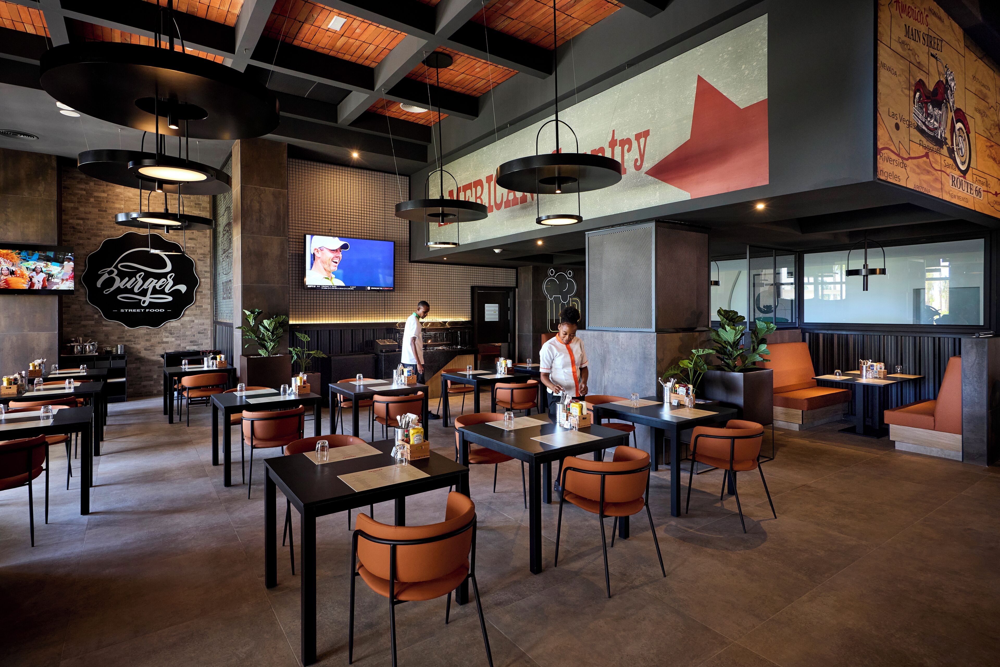Ein Restaurantinneres mit Tischen, Stühlen und einem großen Bildschirm, der ein Programm zeigt.