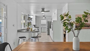 A modern kitchen with white cabinets, a central island, and a dining area with a wooden table and two stools. - Boho Chic, Mtn Preserve Hike, Pool, & Grille! (phoenix)