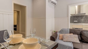 Un coin repas avec une table dressée pour deux personnes, un canapé avec des coussins et un climatiseur fixé au mur.