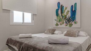 Une chambre avec deux lits, une fenêtre et une peinture murale représentant des cactus et des fleurs.