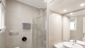 Une salle de bain moderne comprenant des toilettes, une douche à parois de verre, un lavabo avec un miroir et une serviette accrochée au mur.