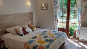 Un dormitorio con cama, mesita de noche, lámpara de pared, ventana con cortinas y una planta en maceta.