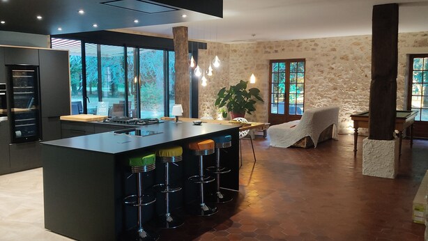 Una cocina moderna con una isla grande, taburetes de bar y un comedor con una silla.