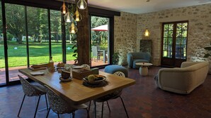Comedor con mesa de madera, sillas e iluminación colgante. Se ve un jardín a través de amplias ventanas.