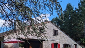 Un edificio de piedra con un patio cubierto, mobiliario exterior y un muro de piedra.