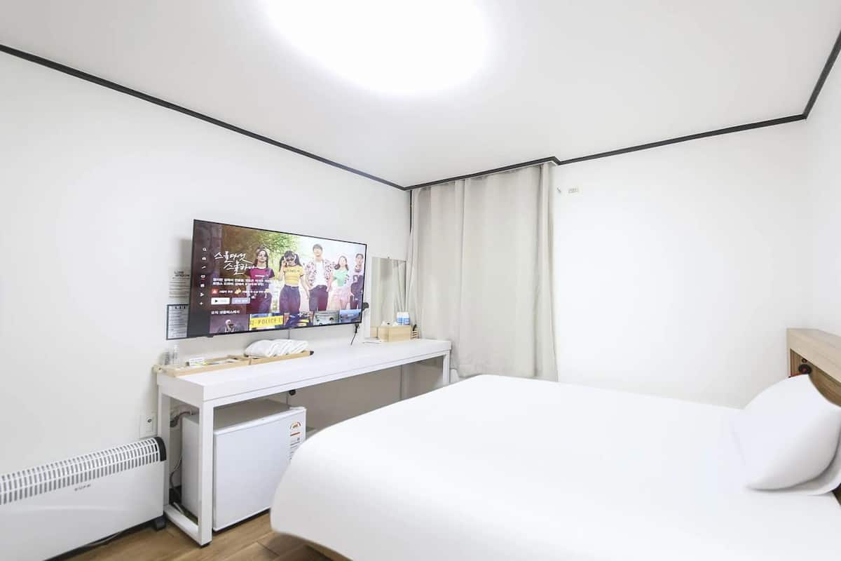 Ein Hotelzimmer mit Bett, Wandfernseher, kleinem Schreibtisch und Heizung.