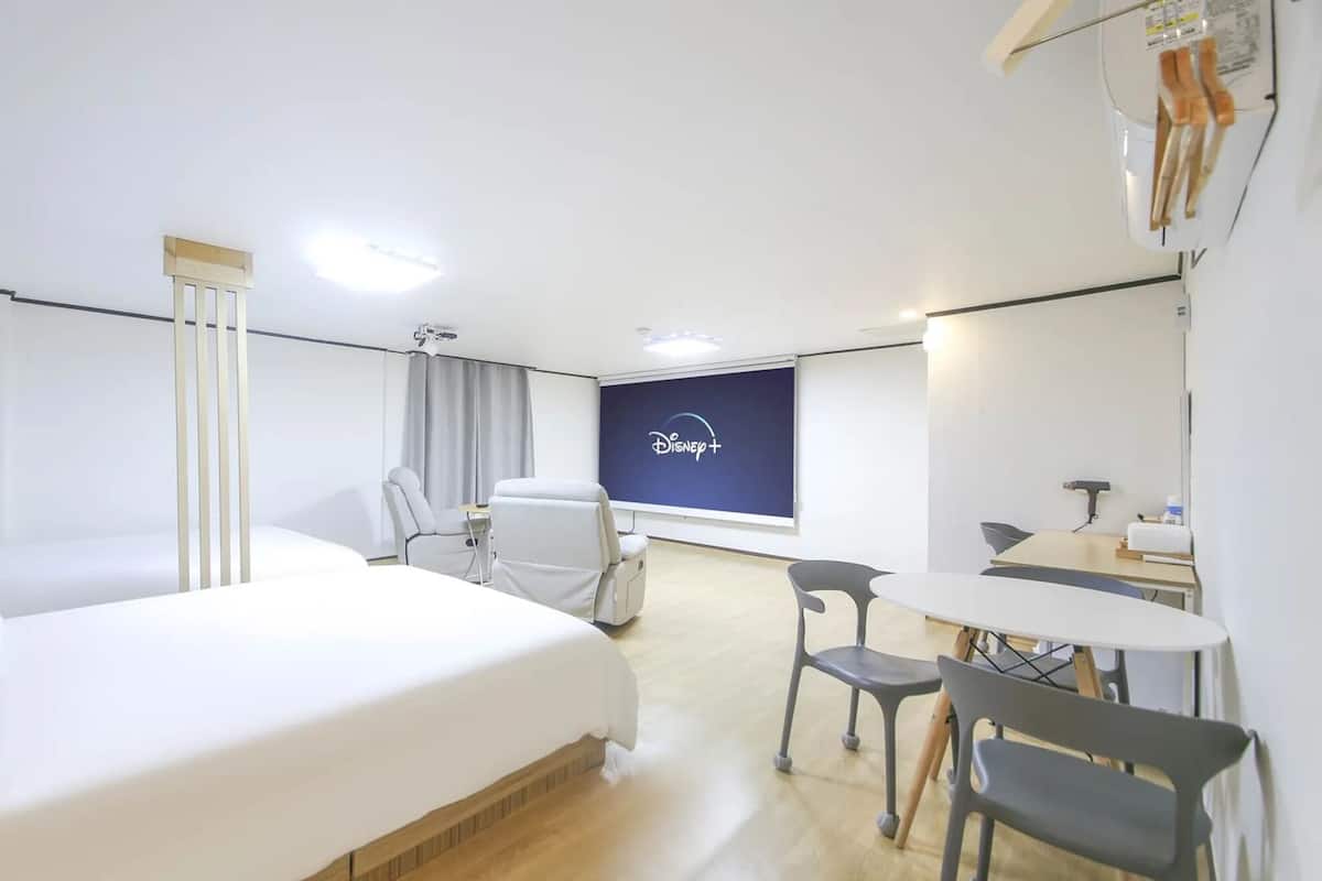 Ein Hotelzimmer mit einem großen Bett, einem Schreibtisch, einem Stuhl und einem Fernseher, der 'Disney+' anzeigt.