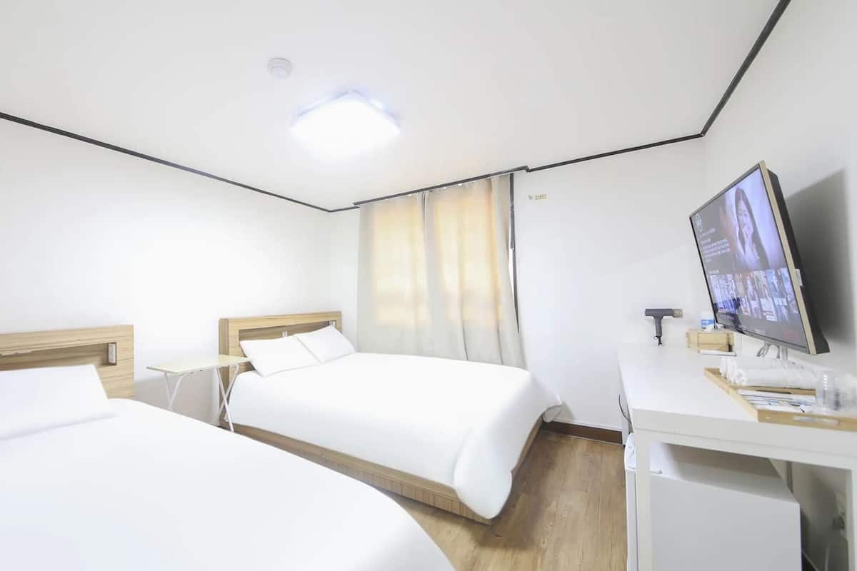 Ein Hotelzimmer mit zwei Betten, einem Schreibtisch mit Fernseher und einem kleinen Tisch.