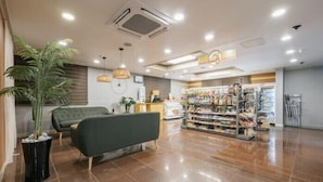 A spacious lobby with a green sofa, a large potted plant, and a well-lit area with ceiling lights and a visible air conditioning unit.