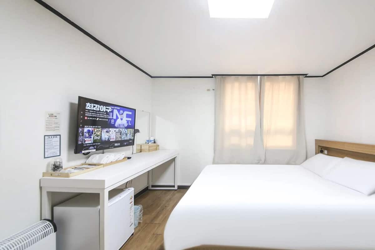 Ein Hotelzimmer mit Bett, Schreibtisch mit Computer, Fernseher an der Wand und einem Fenster mit Vorhängen.