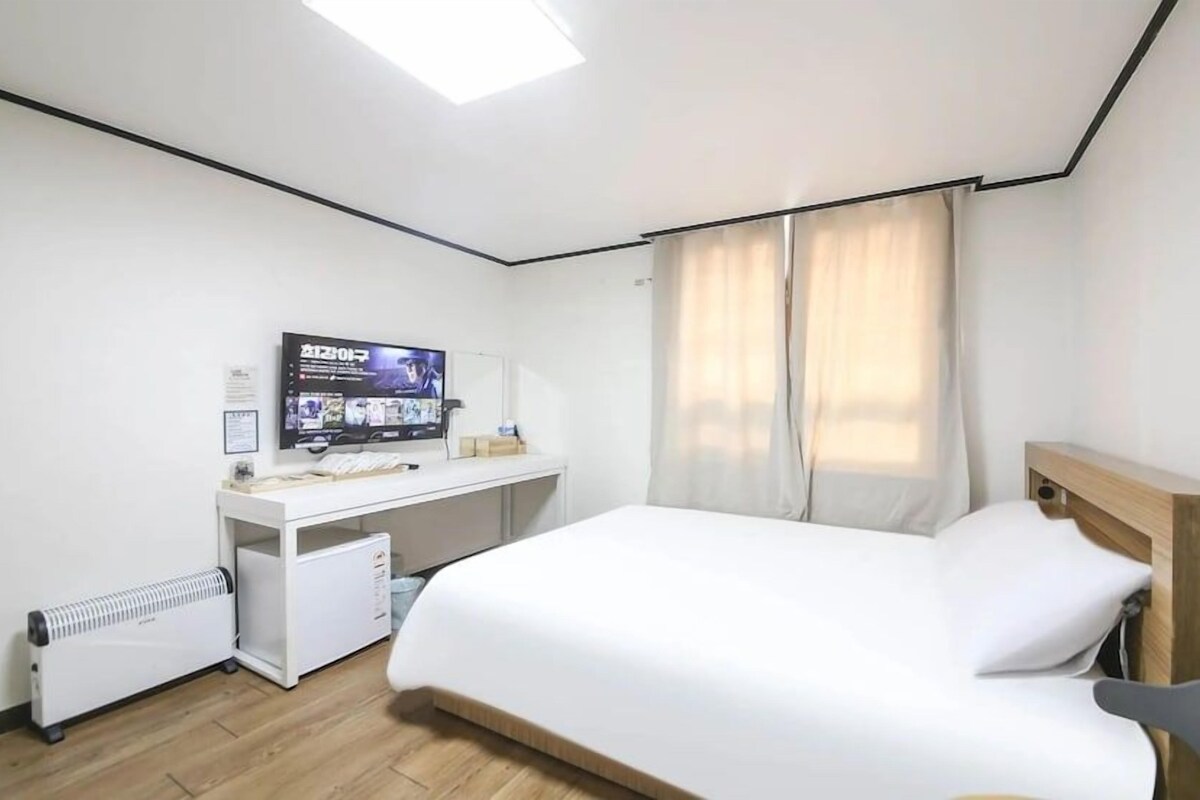 Ein Hotelzimmer mit einem Bett, einem Schreibtisch mit Computer, einem Fernseher und einem Fenster mit Vorhängen.